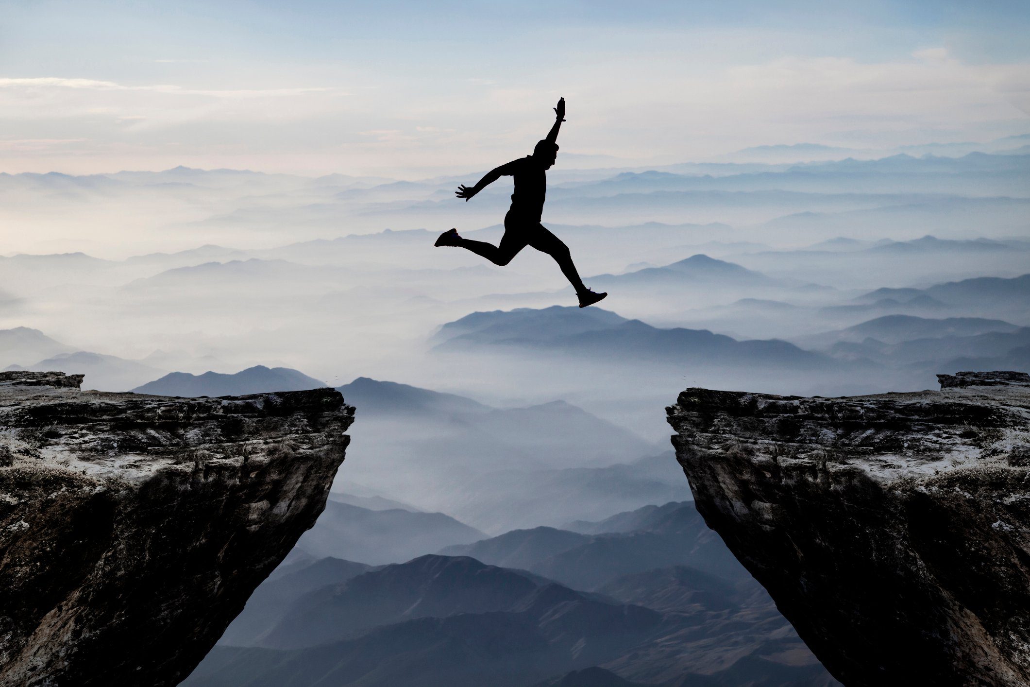 Silhouette of man jumping from one cliff to another cliff with excitement Why Job Hopping is Essential for Personal Growth